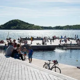 Ludzie odpoczywają i kąpią się na drewnianych pomostach w Oslo. Jak dojechać do fiordów? To miejsce jest idealne na letni relaks.
